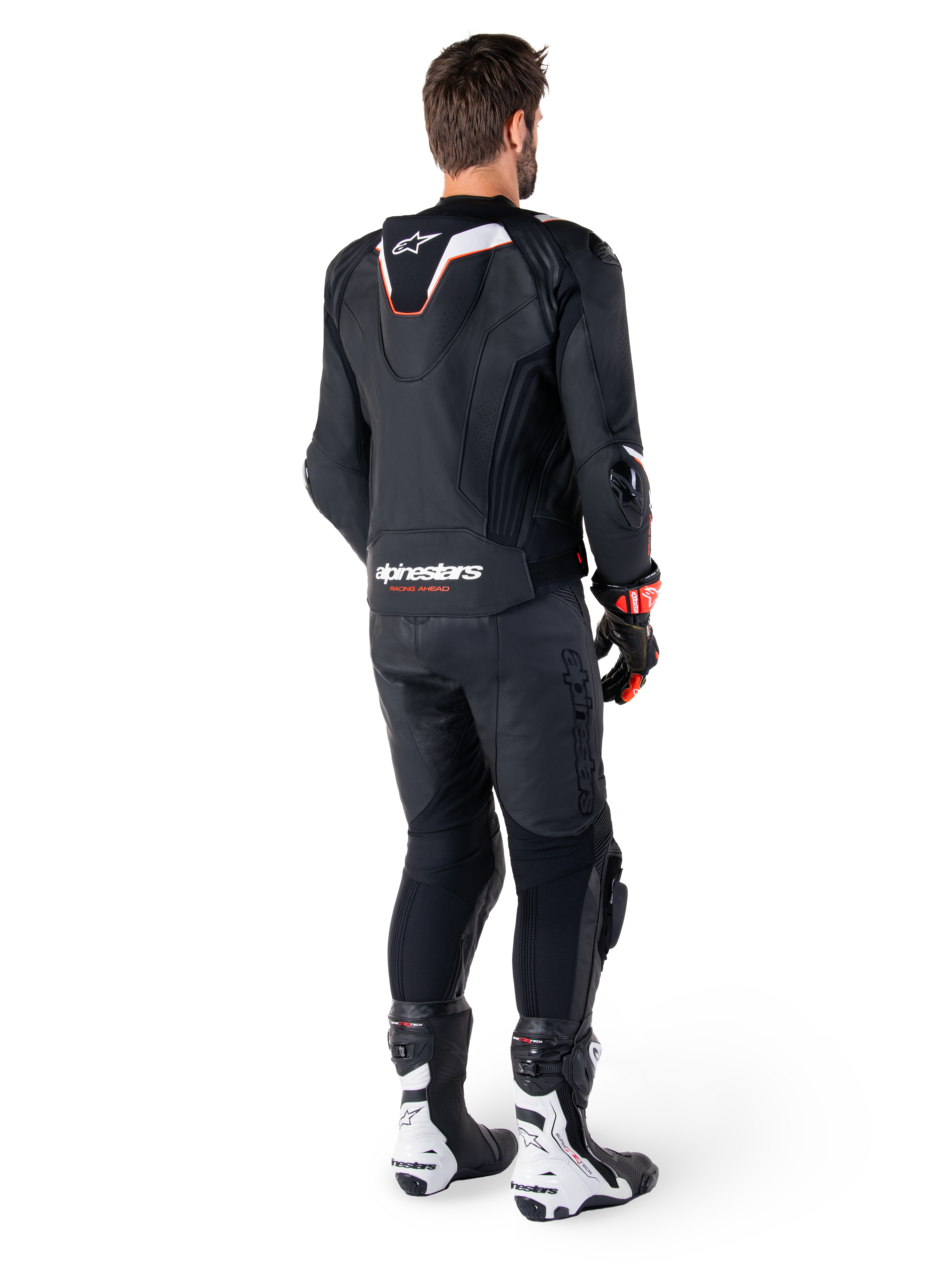 Set bagfra af en kører iført Alpinestars Missile V3 Ignition læderjakke i sort, med en slank sport Aero-hump med hvide og røde detaljer, Alpinestars-branding på den nederste del af ryggen, kombineret med matchende sorte læderbukser og sort-hvide racingstøvler, professionelt sportsudstyr til kørsel