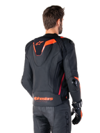 Alpinestars Missile V3 Ignition læderjakke, racing sport jakke til mænd, sort med Red Fluo-detaljer, set bagfra med den slanke aerodynamiske sport-hump og Alpinestars-branding på den nederste del af ryggen, båret med sorte læderbukser og racing-handsker, strømlinet professionelt motorsport-design