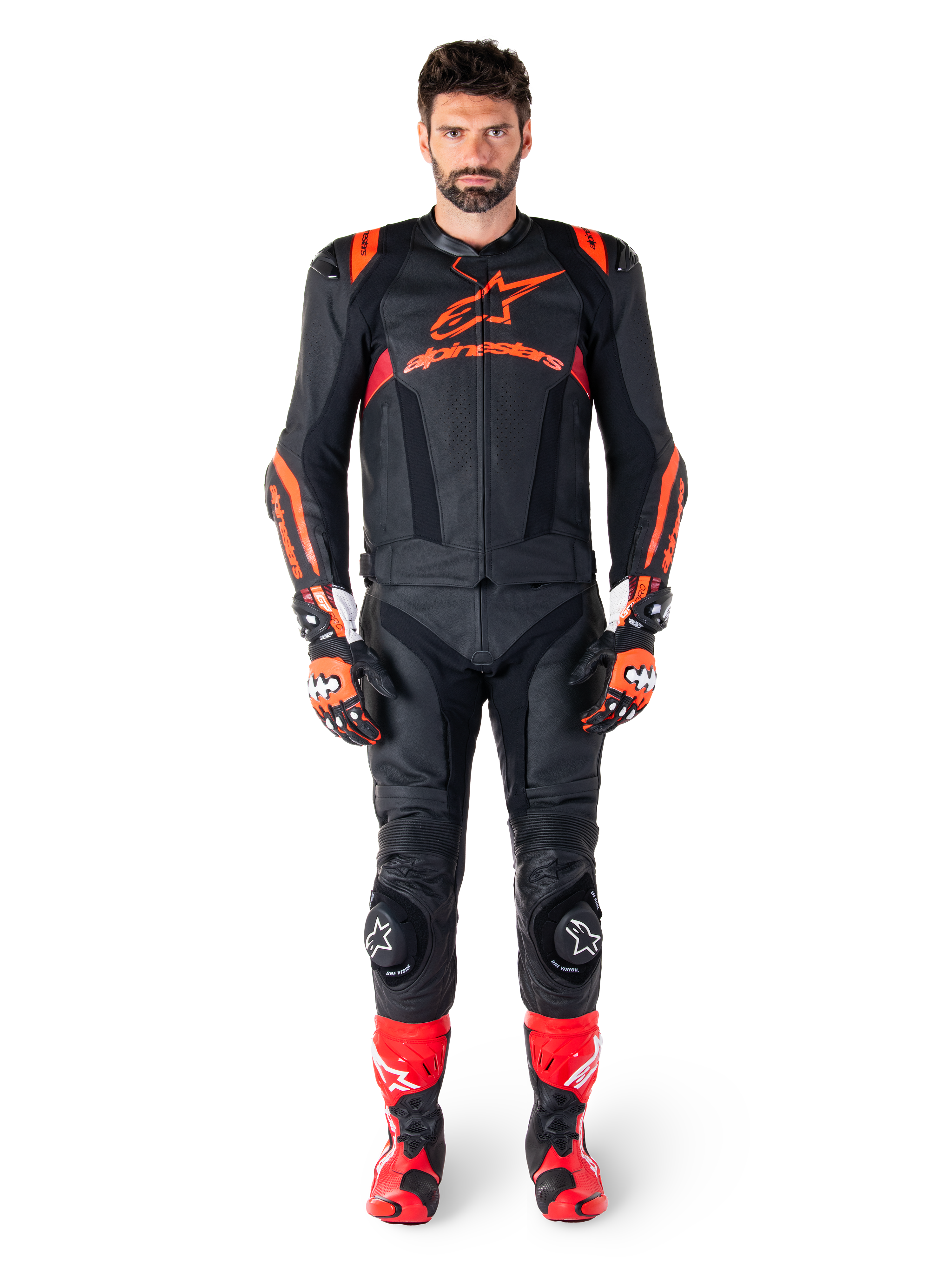 Mandlig model iført Alpinestars Missile V3 Ignition læderjakke i sort, rød fluo og mørkerød, komplet motorcykel-racerudstyr inklusive matchende læderbukser, racerhandsker og støvler, med tydeligt Alpinestars-logo på brystet, frontvendt positur, professionelt sportskøreudstyr