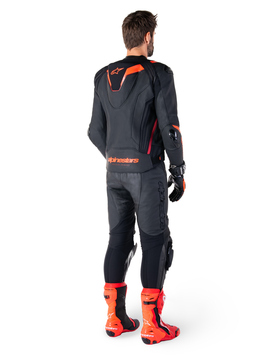 Alpinestars Missile V3 Ignition Læderjakke, racing sport motorcykeljakke, sort og rød fluo, set bagfra af en rytter iført et komplet racing-outfit med matchende læderbukser, handsker og røde støvler, med en sport Aero-hump og tydelig branding på den nederste del af ryggen.