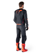 Alpinestars Missile V3 Ignition Læderjakke, racing sport motorcykeljakke, sort og rød fluo, set bagfra af en rytter iført et komplet racing-outfit med matchende læderbukser, handsker og røde støvler, med en sport Aero-hump og tydelig branding på den nederste del af ryggen.