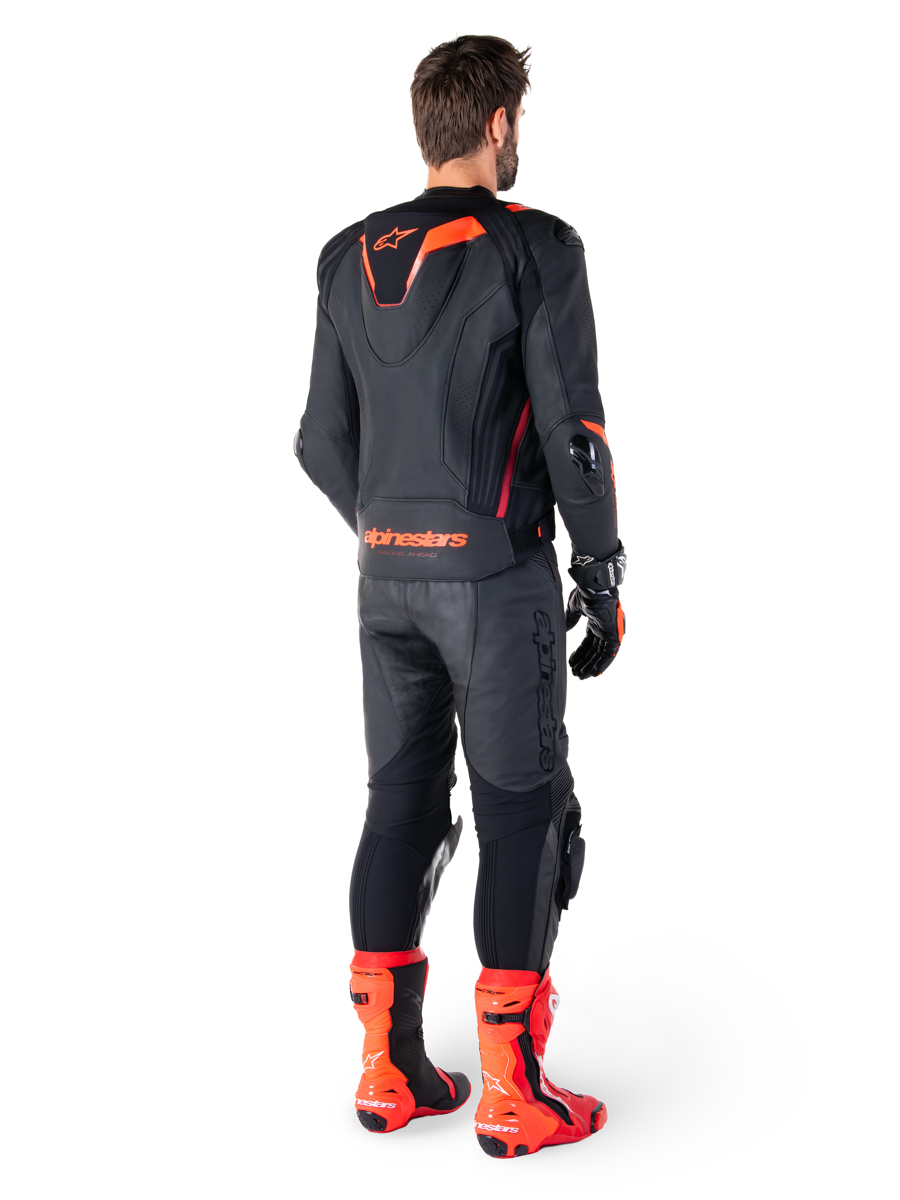 Alpinestars Missile V3 Ignition Læderjakke, racing sport motorcykeljakke, sort og rød fluo, set bagfra af en rytter iført et komplet racing-outfit med matchende læderbukser, handsker og røde støvler, med en sport Aero-hump og tydelig branding på den nederste del af ryggen.