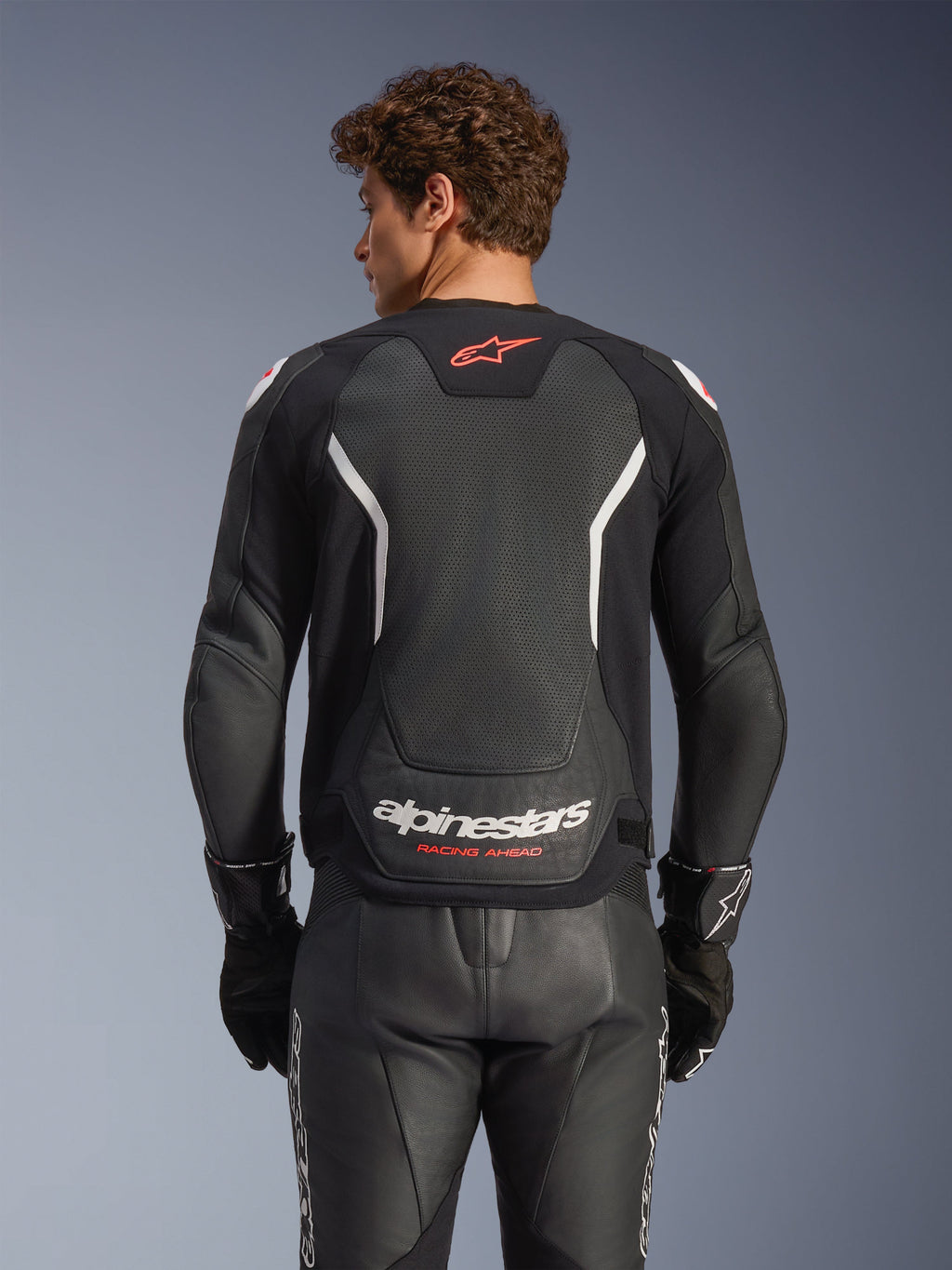 Alpinestars GP Force V2 Air læderjakke, sort med hvide og røde detaljer, bagfra set med perforeret læderrygpanel, hvid Alpinestars-branding og røde logodetaljer, båret med matchende sorte læderracerbukser og handsker