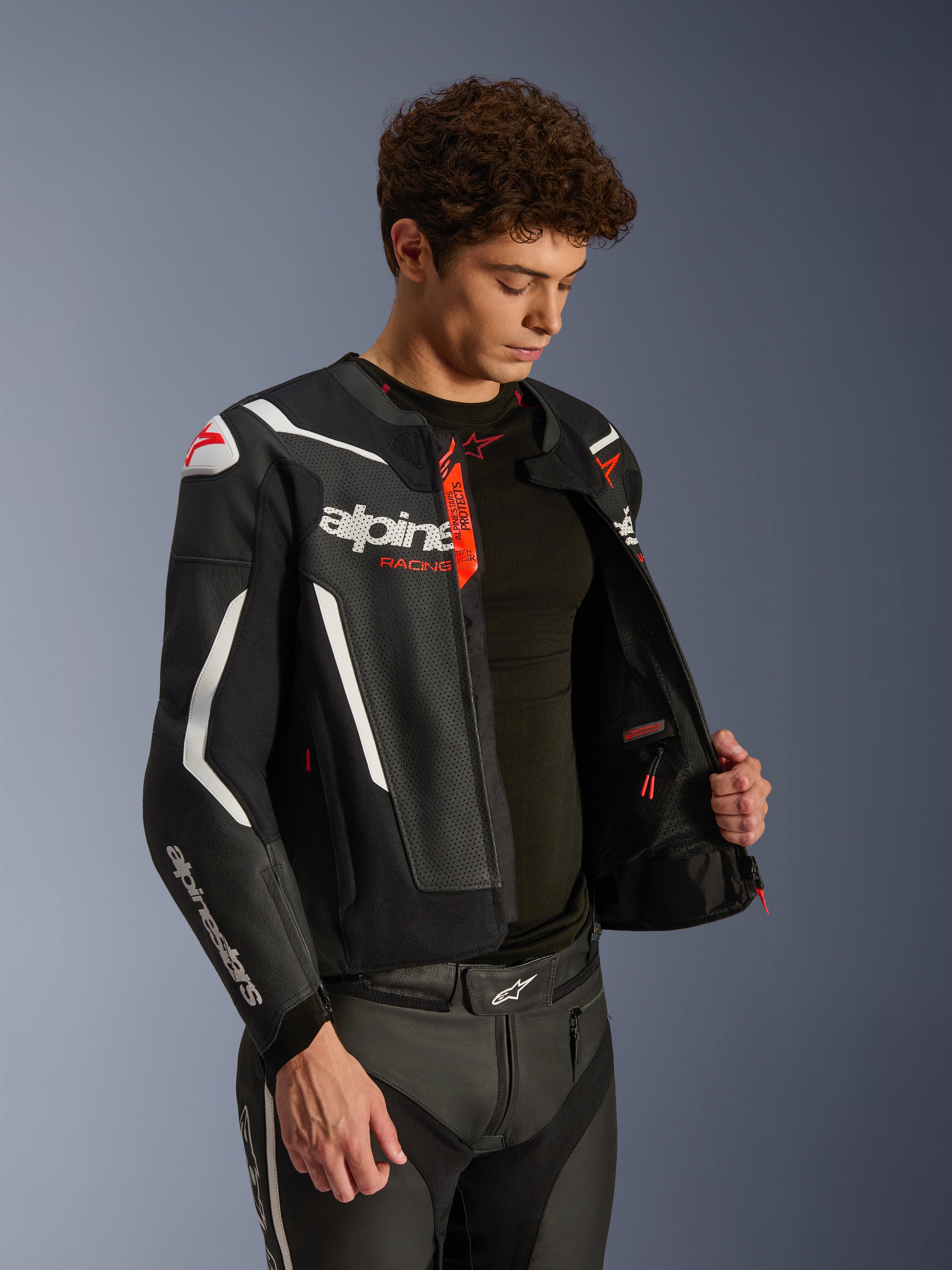 Alpinestars GP Force V2 Air læderjakke, sort og hvid med røde detaljer, perforeret læderkonstruktion, lynet op for at vise indersiden og sort basislag, kombineret med matchende læderbukser, professionelt studiebillede af motorcykeludstyr