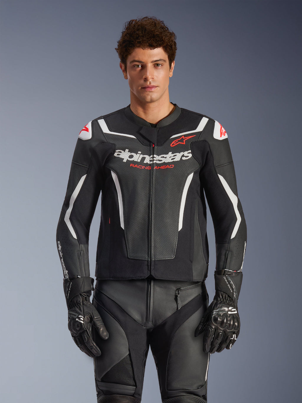 Alpinestars GP Force V2 Air læderjakke, sort med hvide og røde detaljer, model iført perforeret læderjakke med 'alpinestars' og 'RACING AHEAD' branding på brystet, kombineret med matchende racingbukser og handsker, premium sportsmotorcykeludstyr
