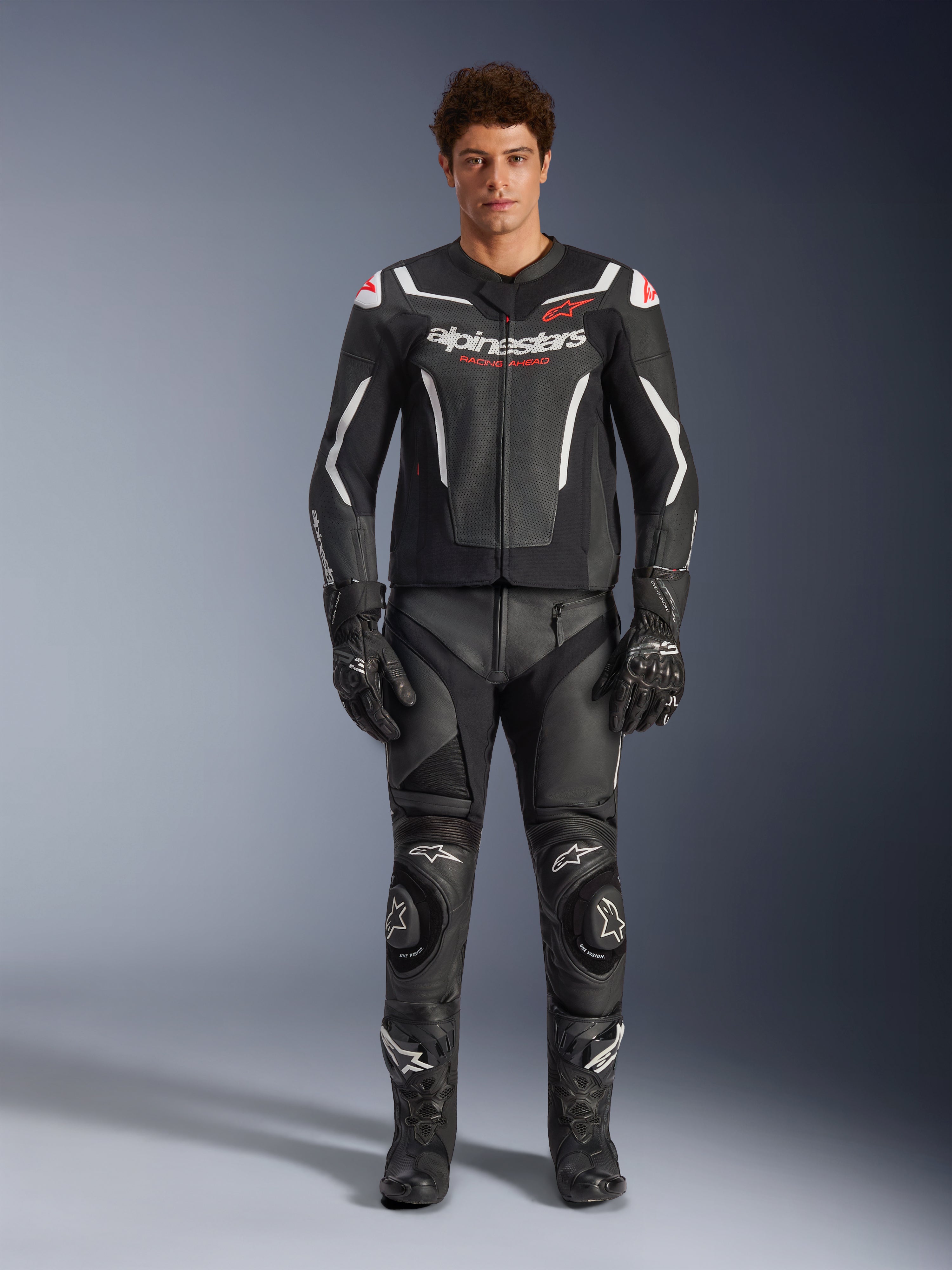 Mandlig model iført Alpinestars GP Force V2 Air læderjakke, sort og hvid, kombineret med matchende læderbukser, handsker og støvler, sporty frontvisning, perforeret læderkonstruktion med hvide detaljer og Alpinestars-logoer