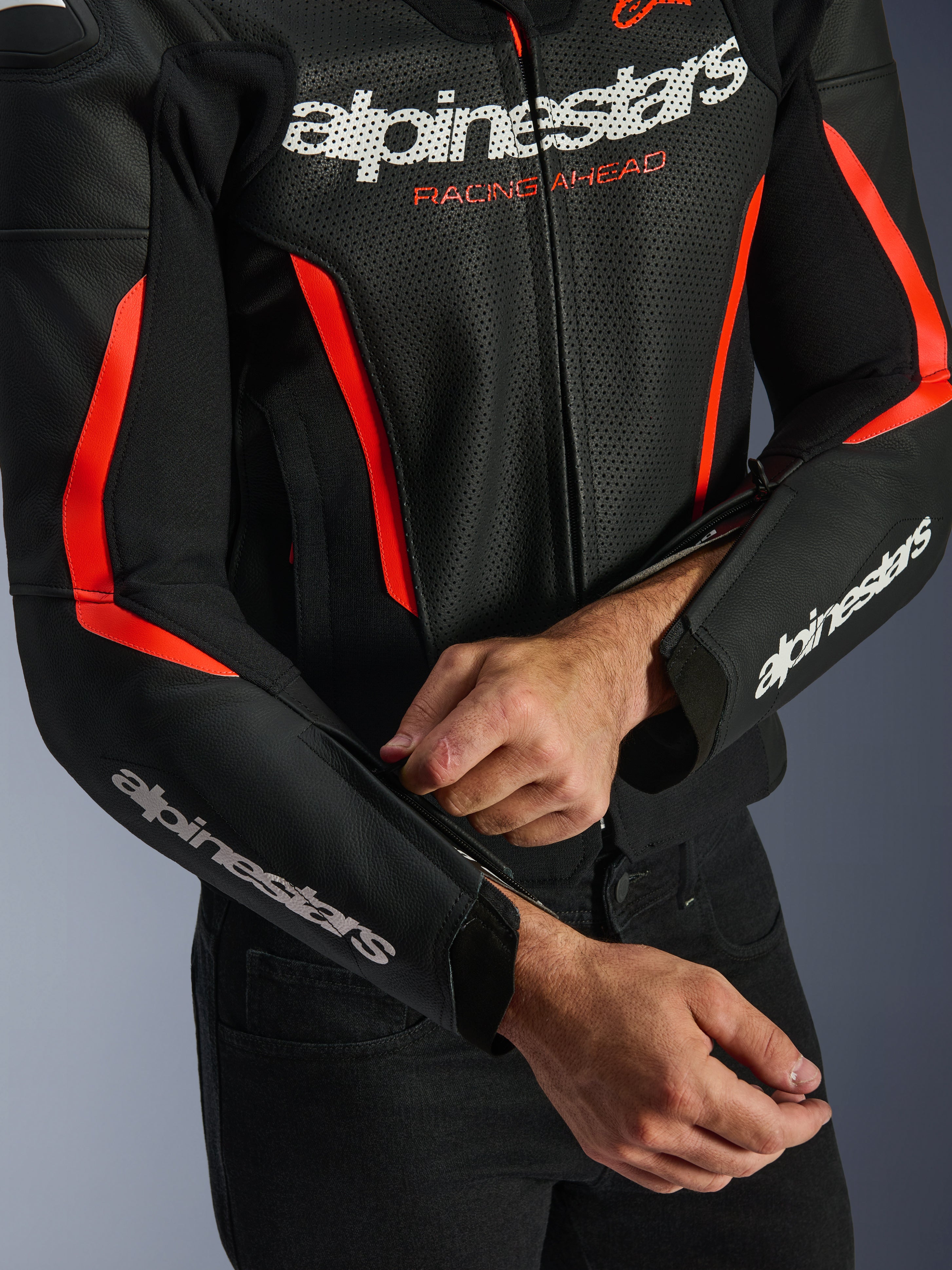 Alpinestars GP Force V2 Air læderjakke i sort og rød fluo, nærbillede der viser den perforerede læderkonstruktion, hvidt branding på bryst og ærmer, og en kører, der justerer lynlåsen på underarmen for en skræddersyet pasform.