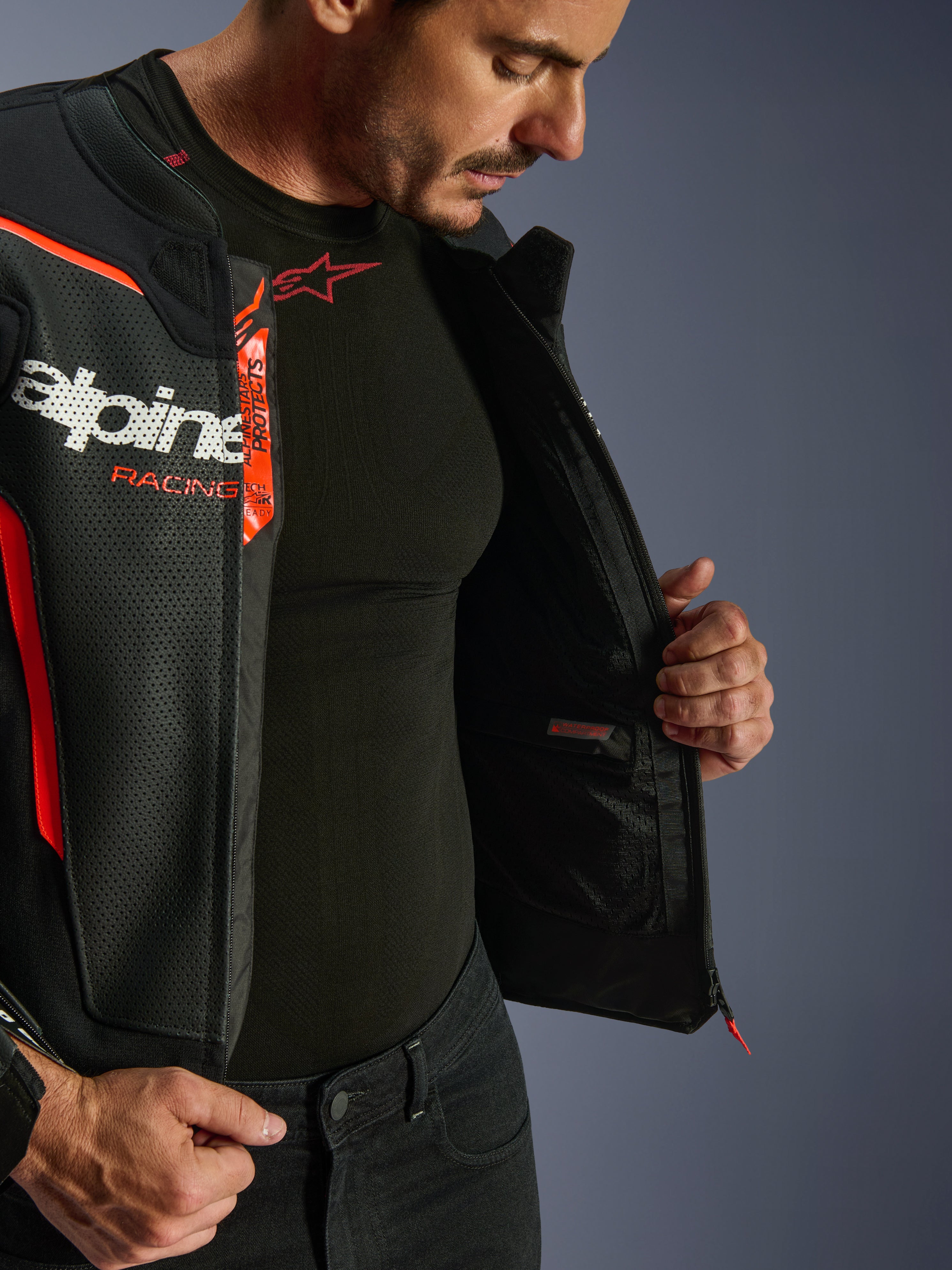 Alpinestars GP Force V2 Air læderjakke, sort og rød fluo, åben for at afsløre indvendig vandtæt lomme og branding, perforeret læder-flerpanelkonstruktion for luftstrøm, båret med sort Alpinestars base layer