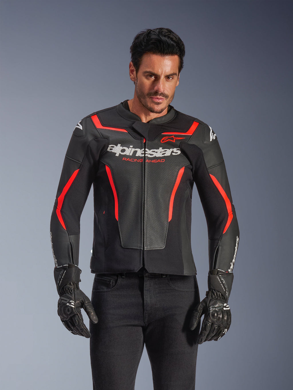 Alpinestars GP Force V2 Air læderjakke, motorcykeljakke til racing, sort og rød fluo, førsteklasses læderkonstruktion med omfattende perforeringer for optimal luftgennemstrømning, båret af en model med sorte handsker og bukser, med markant branding og 'Racing Ahead'-tekst på brystet