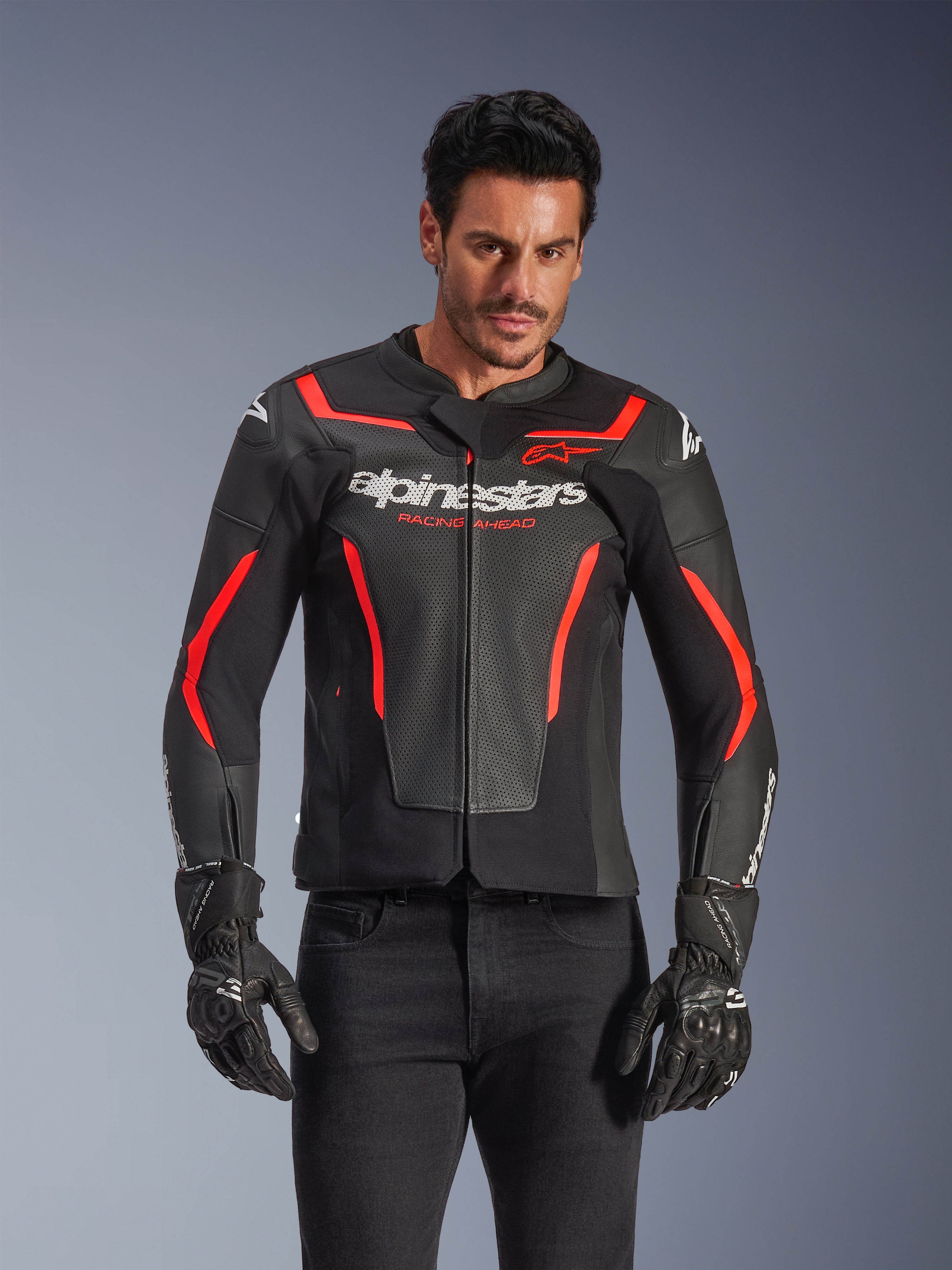 Alpinestars GP Force V2 Air læderjakke, motorcykeljakke til racing, sort og rød fluo, førsteklasses læderkonstruktion med omfattende perforeringer for optimal luftgennemstrømning, båret af en model med sorte handsker og bukser, med markant branding og 'Racing Ahead'-tekst på brystet