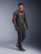 Model iført Alpinestars GP Force V2 Air læderjakke i sort og rød fluo, kombineret med sorte kørebukser, handsker og matchende sneakers, med perforerede læderpaneler og markant hvidt Alpinestars-branding, sports-motorcykeludstyr