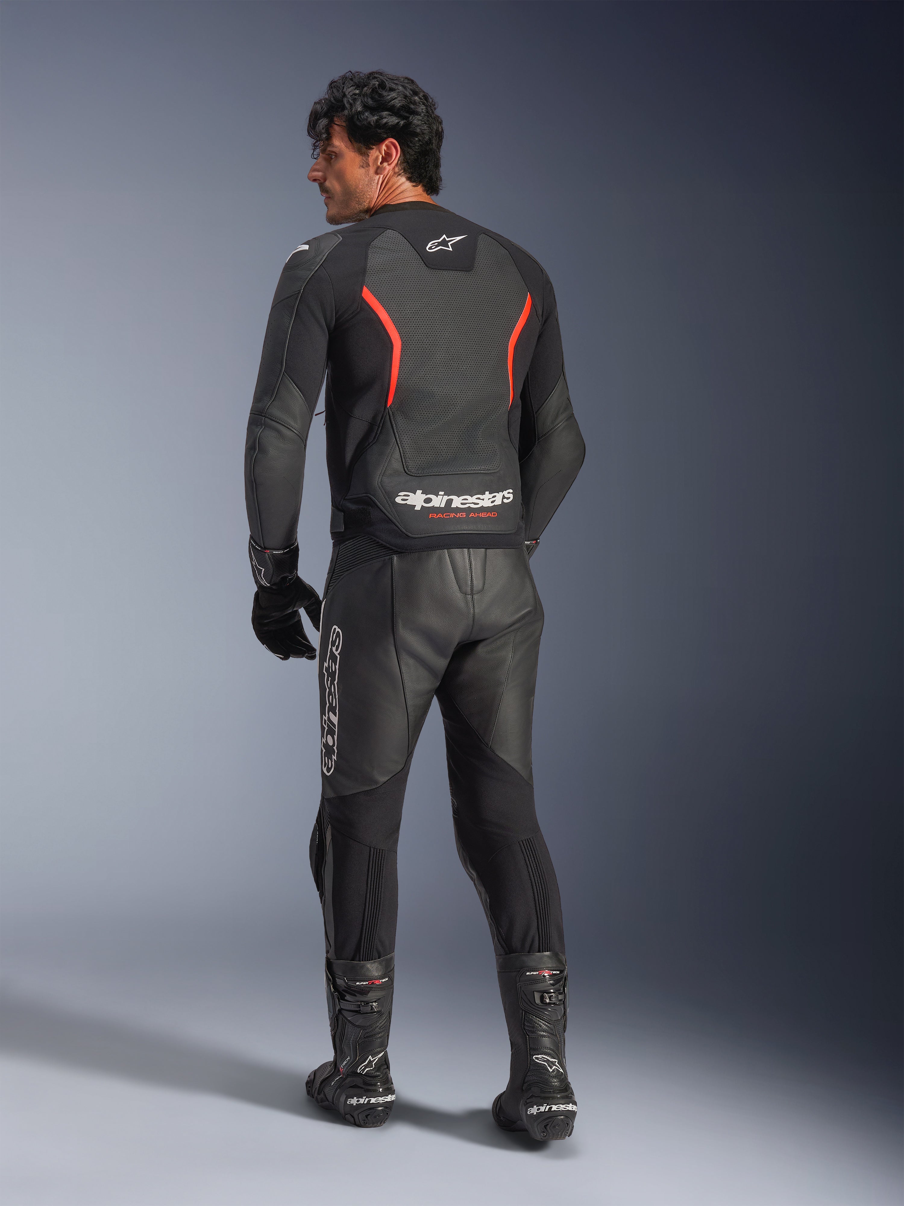 Bagfra-visning af en model iført Alpinestars GP Force V2 Air læderjakke i Black Red Fluo, med perforerede læderpaneler og markant Alpinestars-branding på lænden, stylet med matchende sorte motorcykelbukser og støvler i læder.