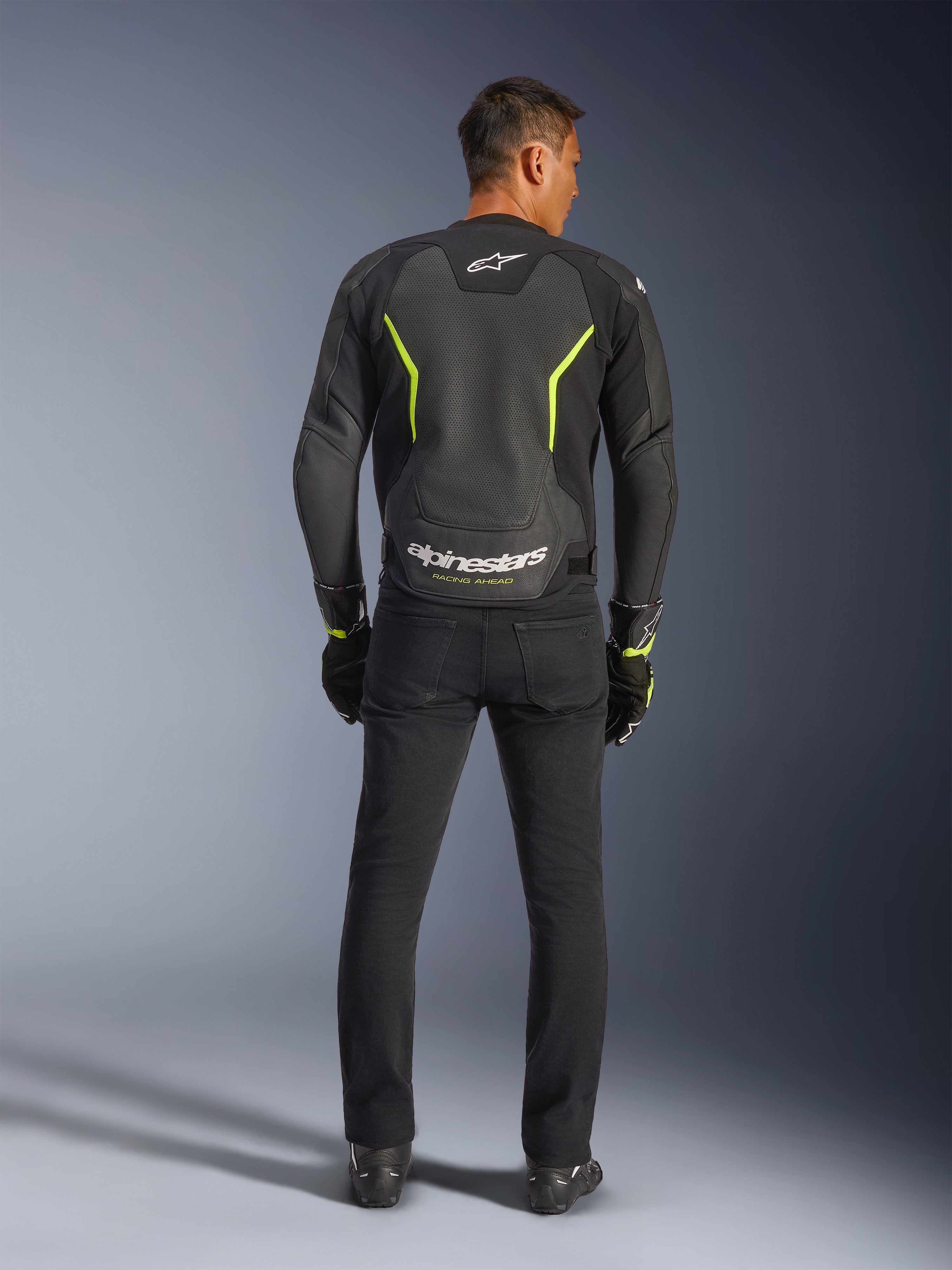 Alpinestars GP Force V2 Air læderjakke, sort og neon gul, rygvisning af model iført sportsmotorcykeljakken, med store perforerede sektioner, neongule detaljer og hvidt 'alpinestars' logo nederst på ryggen, kombineret med sort køreudstyr