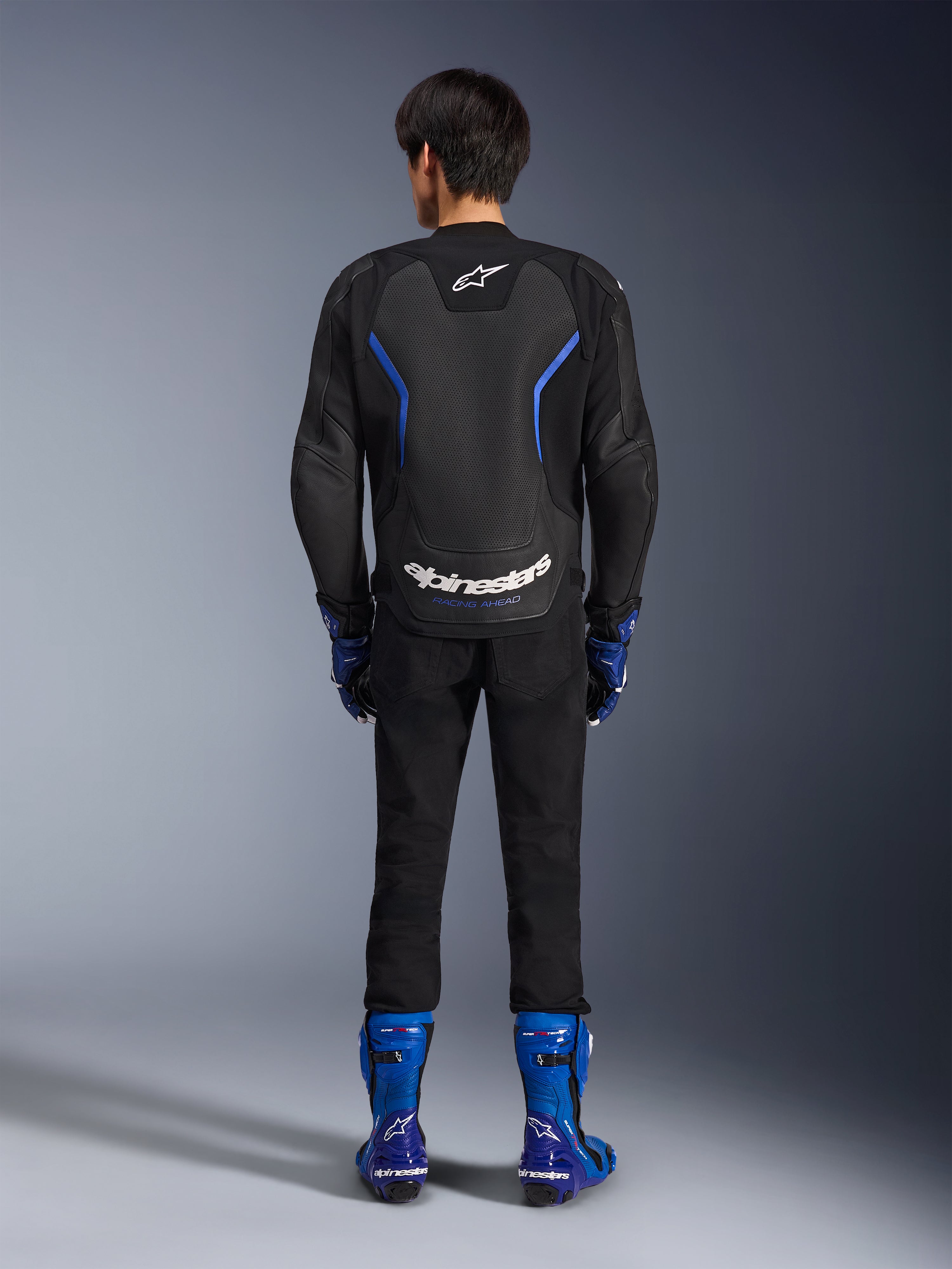Alpinestars GP Force V2 Airflow læderjakke, Black Metallic Blue, set bagfra med perforerede læderpaneler og hvid branding, båret med blå racingstøvler og sorte bukser, sportsmotorcykel-racerudstyr