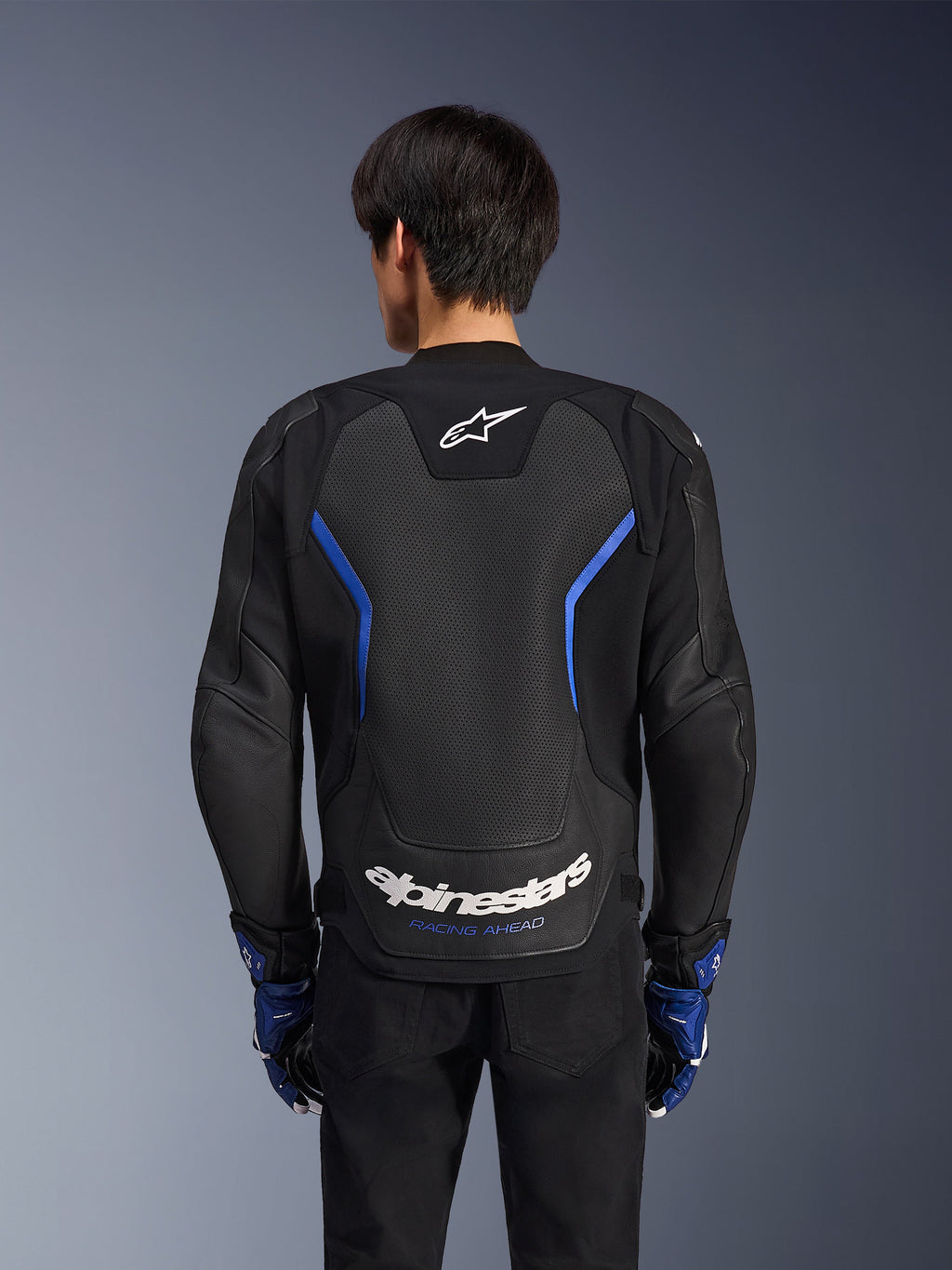 Alpinestars GP Force V2 Airflow læderjakke, Sort Metallic Blå, set bagfra, med et stort perforeret rygpanel til ventilation, blå detaljer og hvid Alpinestars-branding, båret med matchende blå handsker og sorte bukser til sportskørsel.