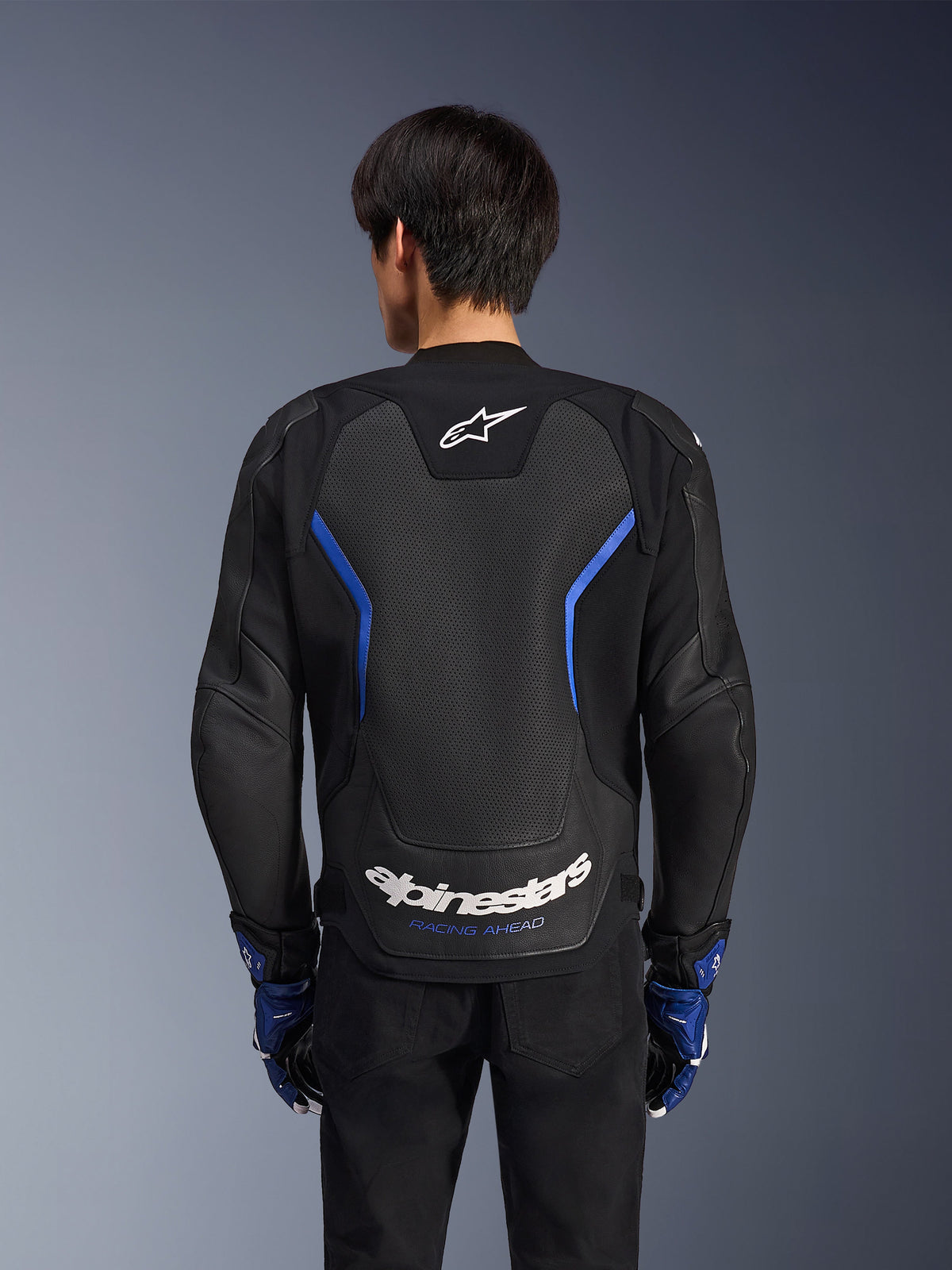 Alpinestars GP Force V2 Airflow læderjakke, Sort Metallic Blå, set bagfra, med et stort perforeret rygpanel til ventilation, blå detaljer og hvid Alpinestars-branding, båret med matchende blå handsker og sorte bukser til sportskørsel.
