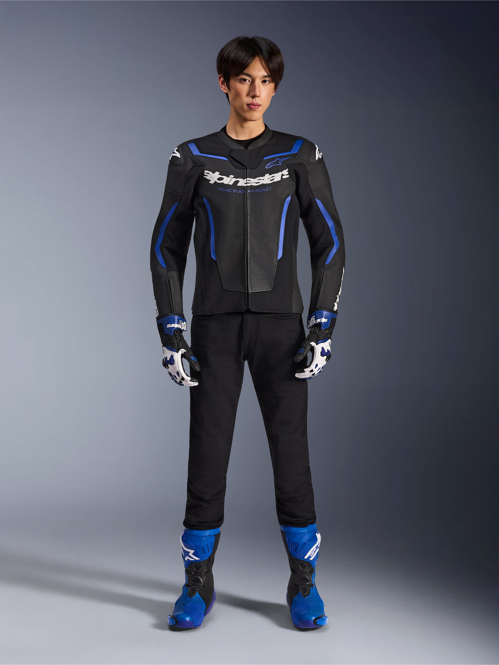 Alpinestars GP Force V2 Airflow læderjakke i Black Metallic Blue, båret med matchende racerhandsker, sorte bukser og blå støvler, professionelt sport-motorcykeludstyr, fuldkropsstudiebillede