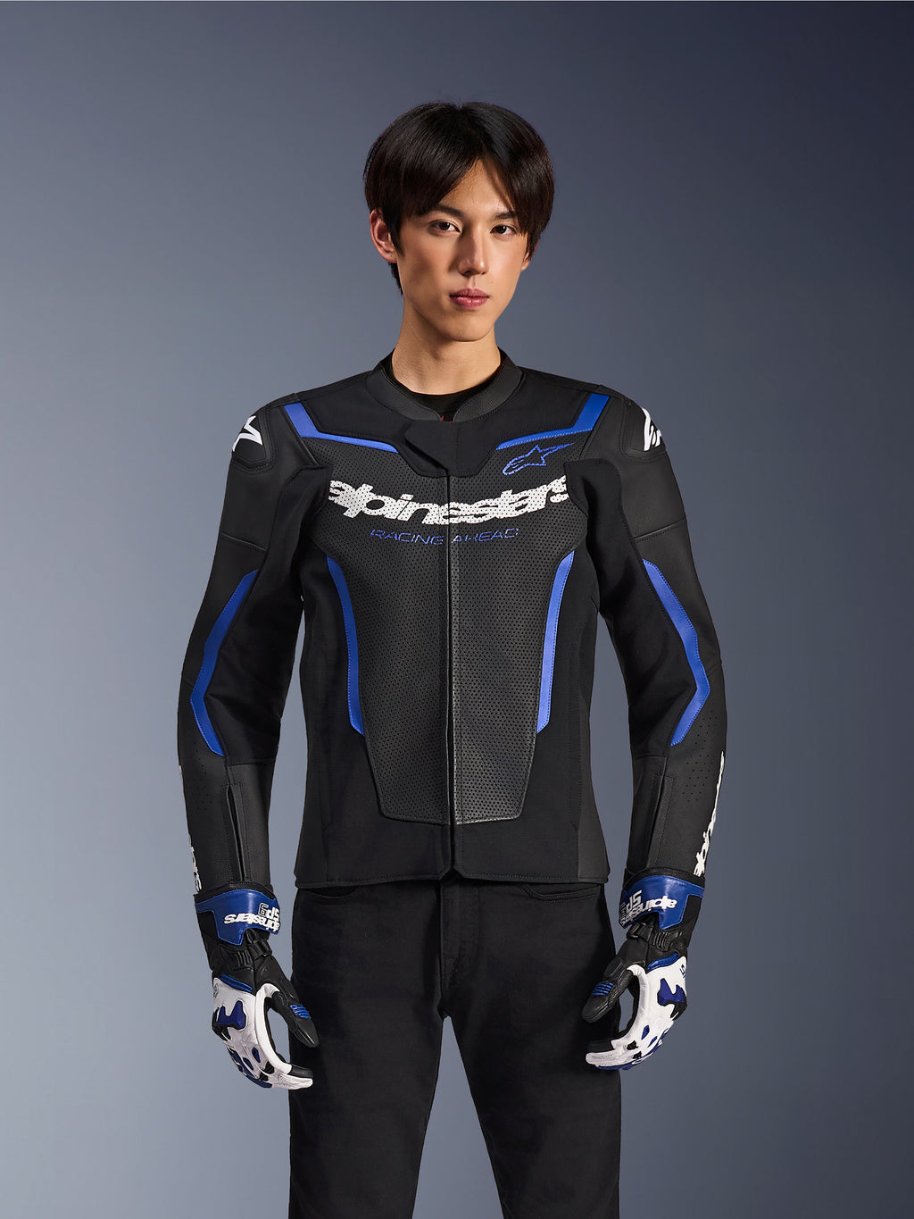 Alpinestars GP Force V2 Airflow læderjakke, sort metallisk blå, motorcykeljakke med perforeret læder og blå detaljer, båret af en model med matchende racerhandsker og sorte bukser, professionelt sportskøreudstyr