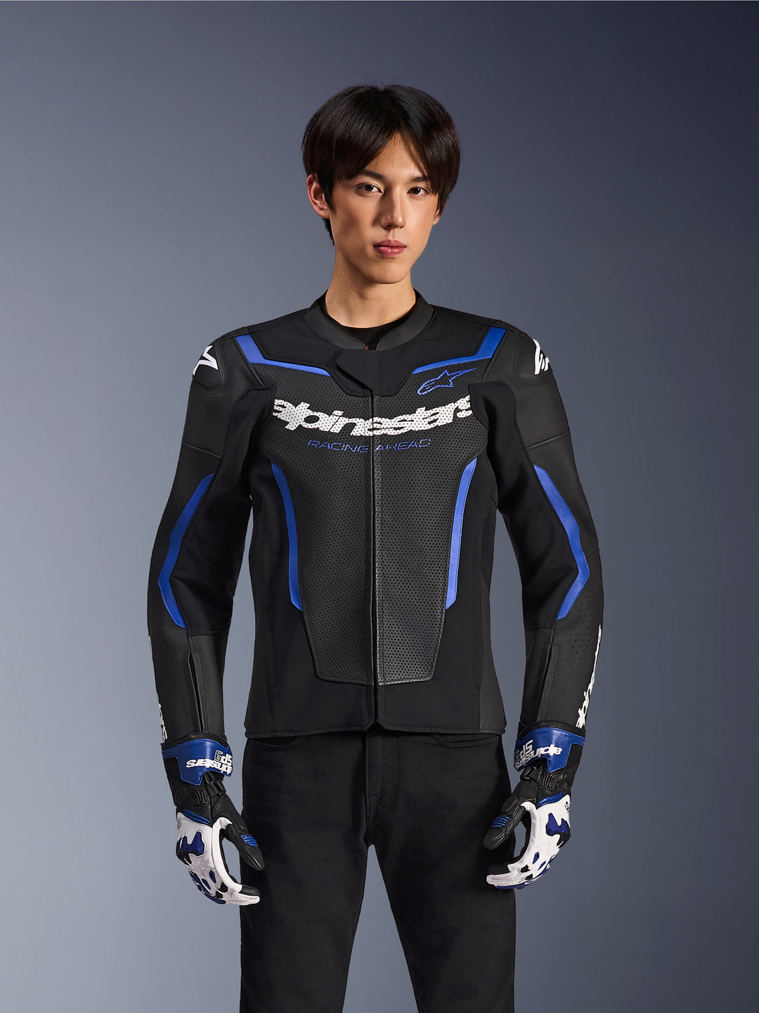 Alpinestars GP Force V2 Airflow læderjakke, sort metallisk blå, motorcykeljakke med perforeret læder og blå detaljer, båret af en model med matchende racerhandsker og sorte bukser, professionelt sportskøreudstyr