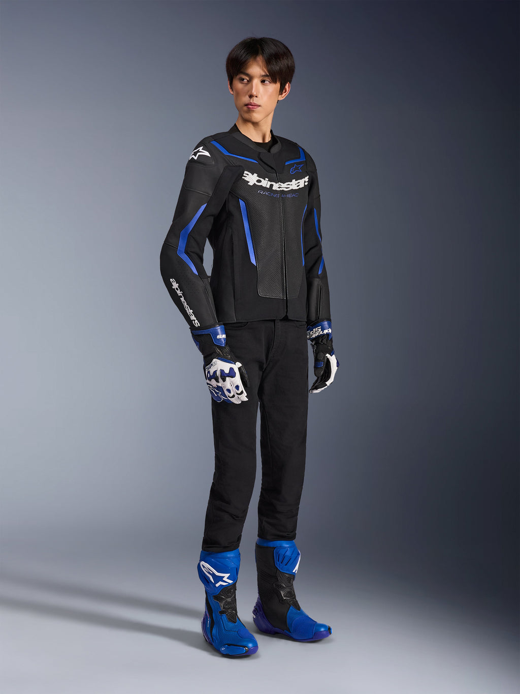 Mandlig kører iført GP Force V2 Airflow-læderjakke i Black Metallic Blue, kombineret med matchende racerhandsker og blå støvler, med perforeret læder og tydelig Alpinestars-branding, professionelt motorcykeludstyr til vejbrug.