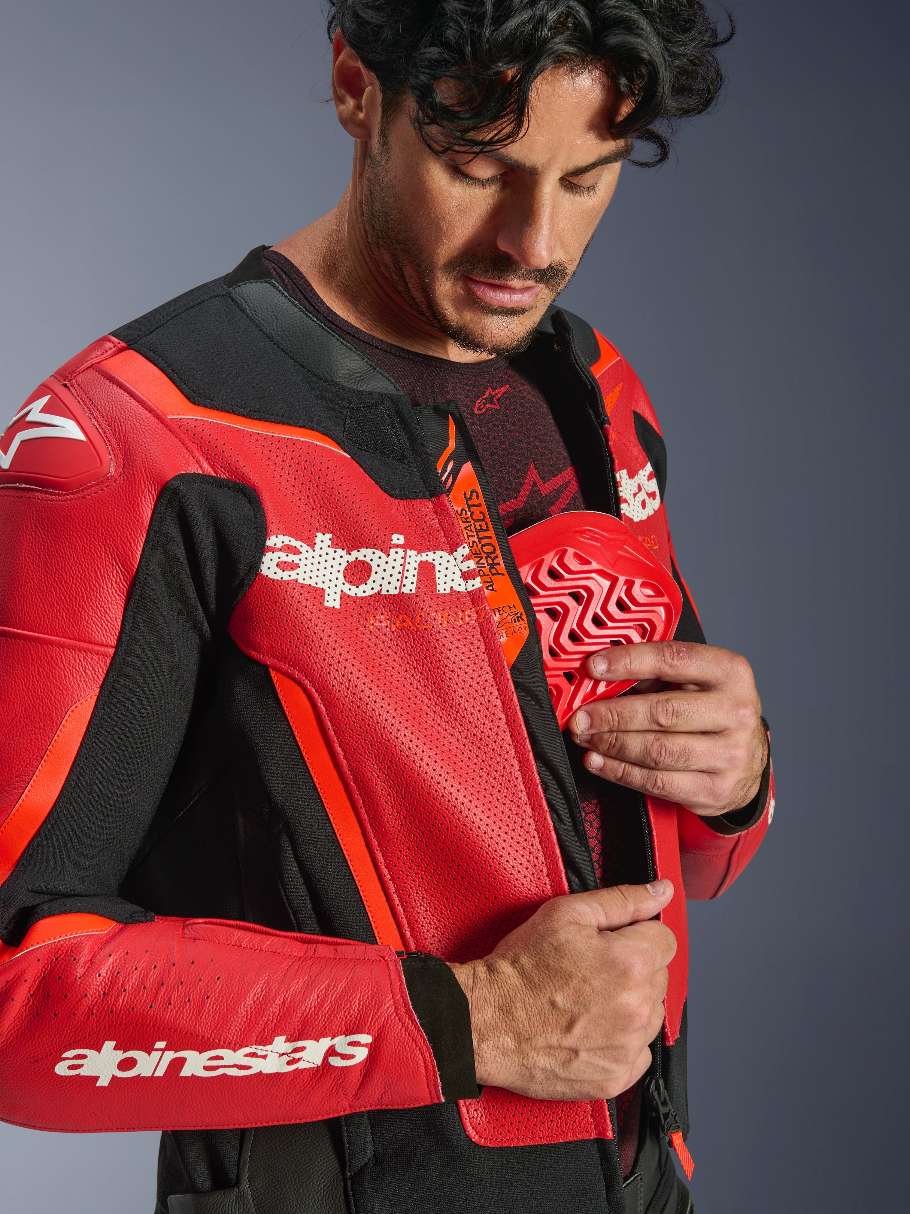 Alpinestars GP Force V2 Air læderjakke, rød og rød fluo, nærbillede af en kører, der indsætter en rød brystbeskytter i den indvendige lomme, med perforeret læder og Tech-Air Ready-logo, førsteklasses sportslig motorcykelbeskyttelse.