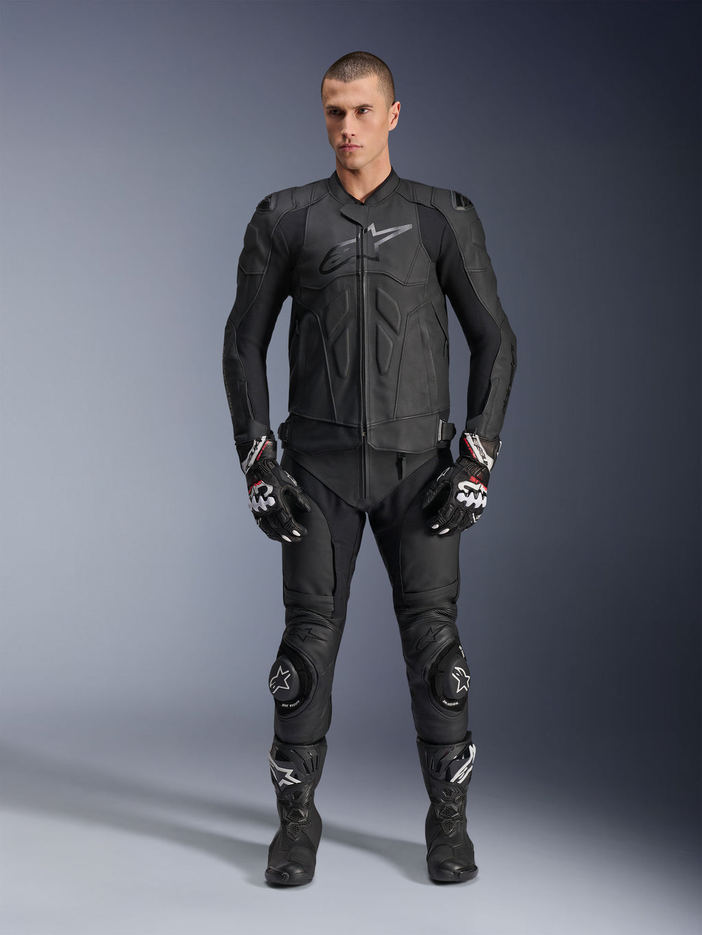 Alpinestars Dusk læderjakke, sort, båret af en mandlig model som en del af et komplet racer-inspireret outfit inklusive matchende læderbukser, handsker og støvler, strømlinet ergonomisk design med beskyttelse ved skuldrene og branding på brystet.