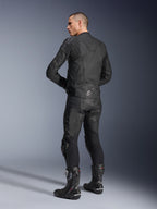Alpinestars Dusk læderjakke, sort, set trekvart bagfra på en model iført matchende læder-motorcykelbukser og performance racing-støvler, med harmonika-strækpaneler i læder, sølvfarvet Alpinestars-stjernelogo på lænden og DUSK-branding øverst på ryggen, professionelt studiobillede.