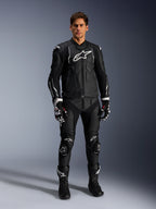 Mandlig model iført Alpinestars Dusk læderjakke i sort og hvid, markante hvide logoer på brystet og skuldrene, matchende sorte motorcykelbukser i læder, sort-hvide handsker og sorte støvler, komplet sports-raceroutfit til vejbrug