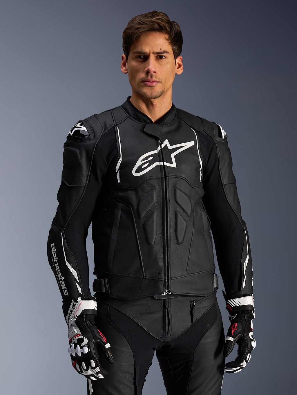 Alpinestars Dusk læderjakke, sort og hvid, motorcykeljakke i læder med polstrede beskyttelsesområder og hvide logoer, båret med sort-hvide racinghandsker med røde detaljer, professionelt sportskøreudstyr