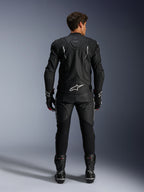 Motorcykelrytter set bagfra iført Alpinestars Dusk læderjakke og Missile V3 læderbukser, komplet sort læderdragt med hvide detaljer, jakken har 'Dusk'-branding og Alpinestars-logo på ryggen, kombineret med sorte racingstøvler og handsker, koordineret motorsport-outfit til vejkørsel.