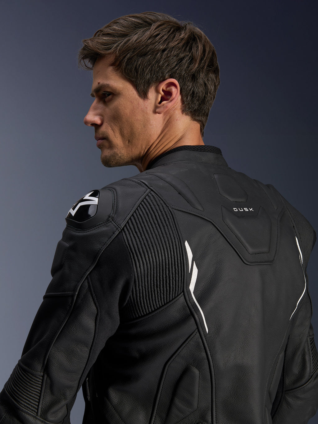 Alpinestars Dusk læderjakke, sort med hvide detaljer, set bagfra på model, med DFS-skulderbeskyttere med Alpinestars-logo, harmonika-læderstrækpaneler for mobilitet og 'DUSK'-branding på den øverste del af ryggen, premium motorcykeljakke i okselæder til vej- og sportskørsel