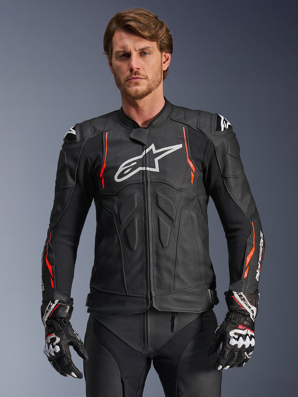 Alpinestars Dusk Airflow læderjakke, sort med rød fluo og hvide detaljer, motorcykel racingjakke i læder, med omfattende perforeringer for ventilation, hvidt logo på brystet og udvendige skulder-sliders, vist på en model med matchende racinghandsker
