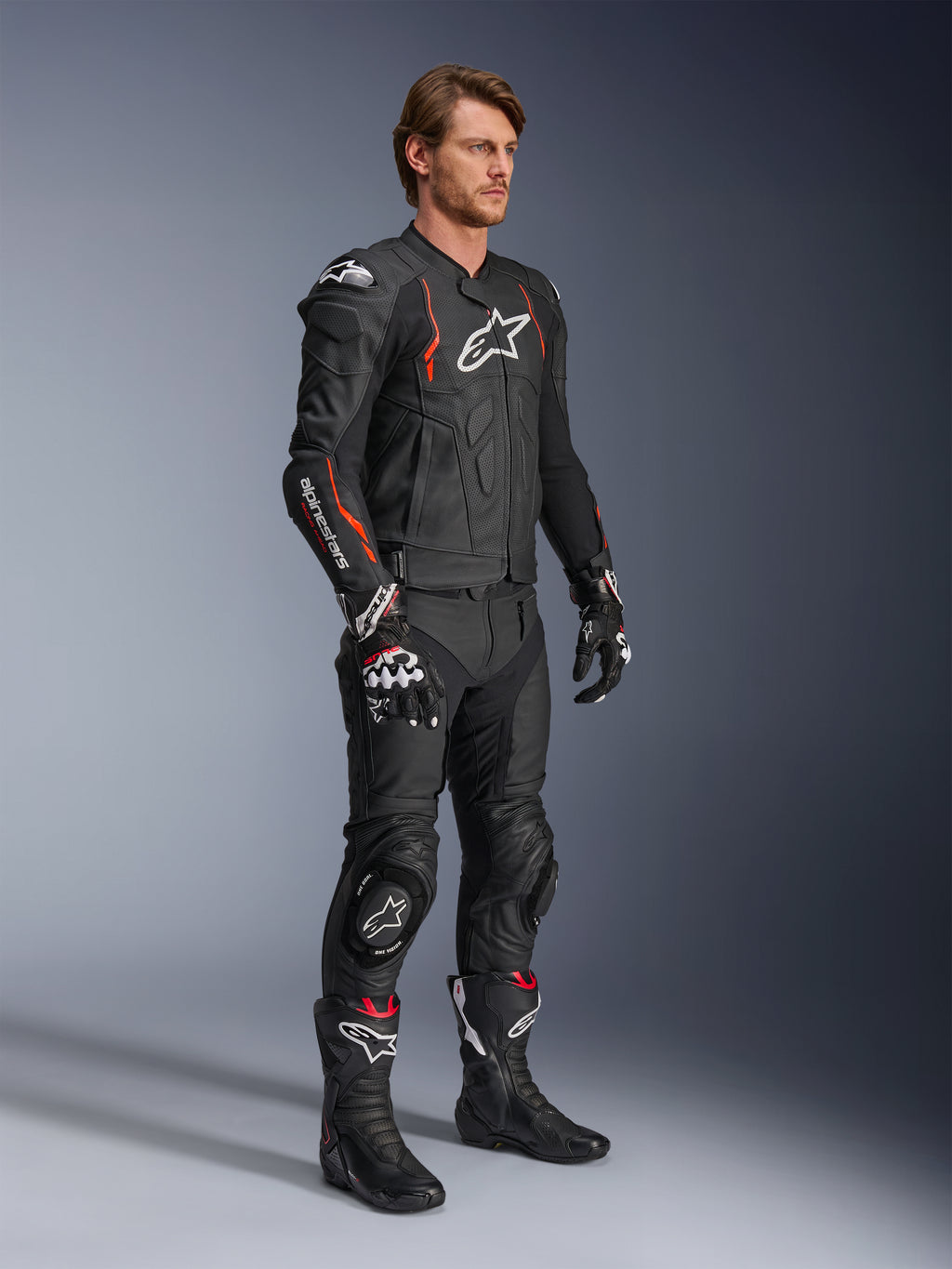 Alpinestars Dusk Airflow læderjakke, sort og rød fluo, båret som en del af et komplet motorcykel-raceroutfit med matchende læderbukser, handsker og støvler, perforeret læderkonstruktion og sporty detaljer