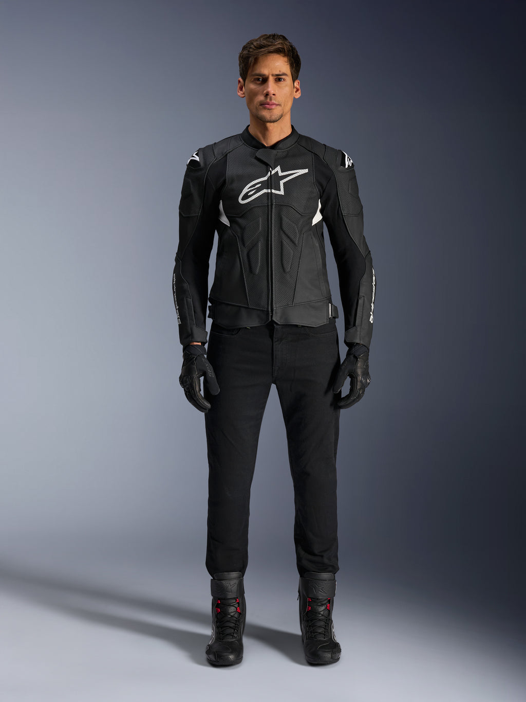 Alpinestars Dusk Airflow læderjakke, sort og hvid, motorcykel læderjakke med perforerede paneler til luftstrøm, hvidt Astars-logo på brystet, båret af en mandlig rytter med sorte bukser, handsker og kørestøvler, professionelt studiebillede af sportsmotorcykeludstyr.
