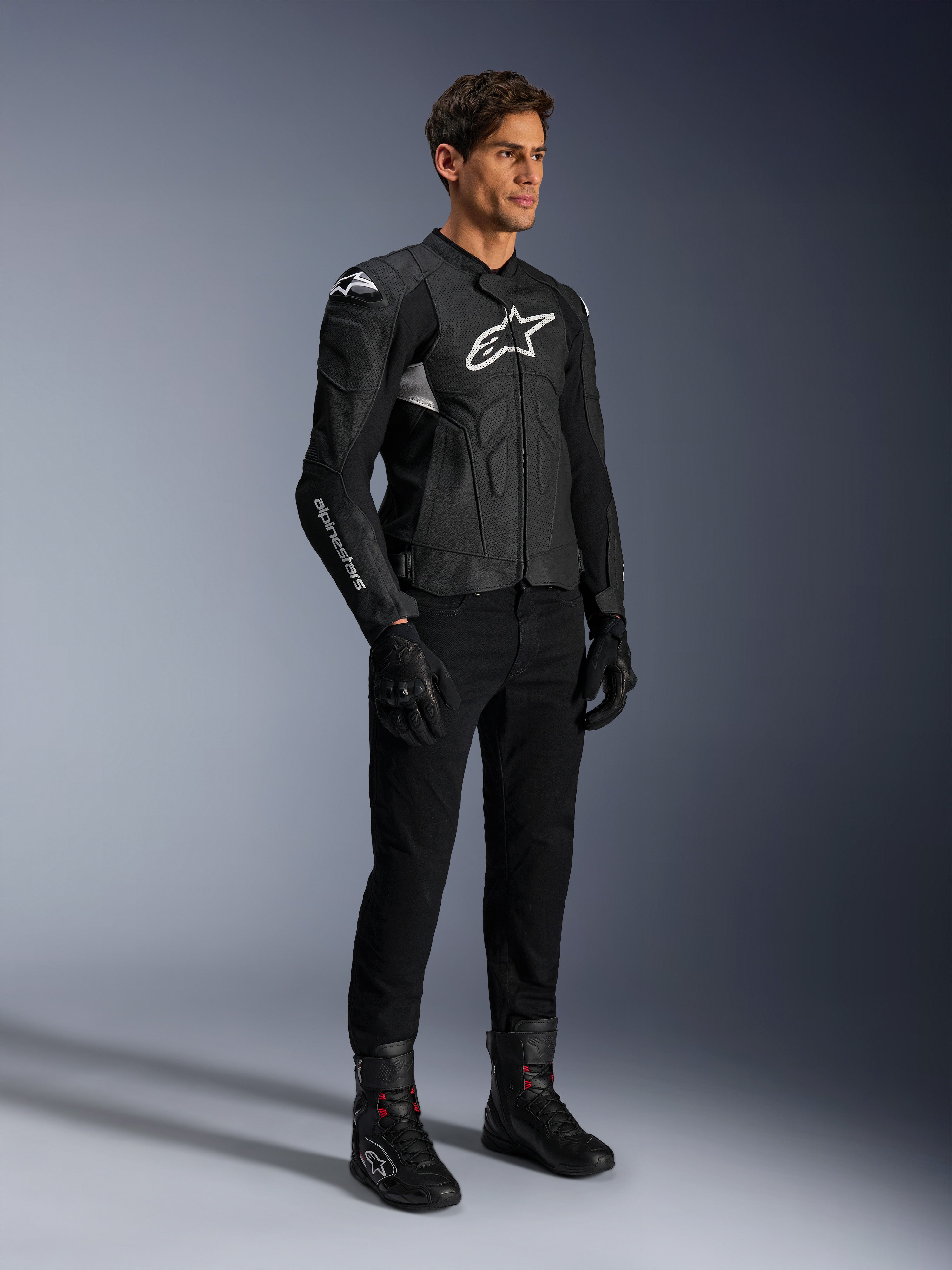 Alpinestars Dusk Airflow læderjakke, sort og hvid, vist med sorte motorcykelbukser, handsker og støvler, med perforerede læderpaneler og hvidt logo, sportslig road racing-stil.