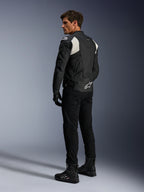 Alpinestars Dusk Airflow læderjakke, sort og hvid, set bagfra af model iført den perforerede læderjakke med matchende sorte bukser og støvler, hvide harmonika-strækpaneler og markant logo på lænden, sporty motorcykeludstyr