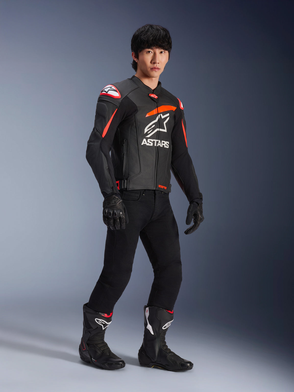 Mandlig kører iført Alpinestars GP Plus R V4 Airflow læderjakke, sort med rød fluo og hvide detaljer, perforeret læder og ASTARS brystlogo, sorte kørebukser og sorte motorcykelstøvler, sports performance-udstyr