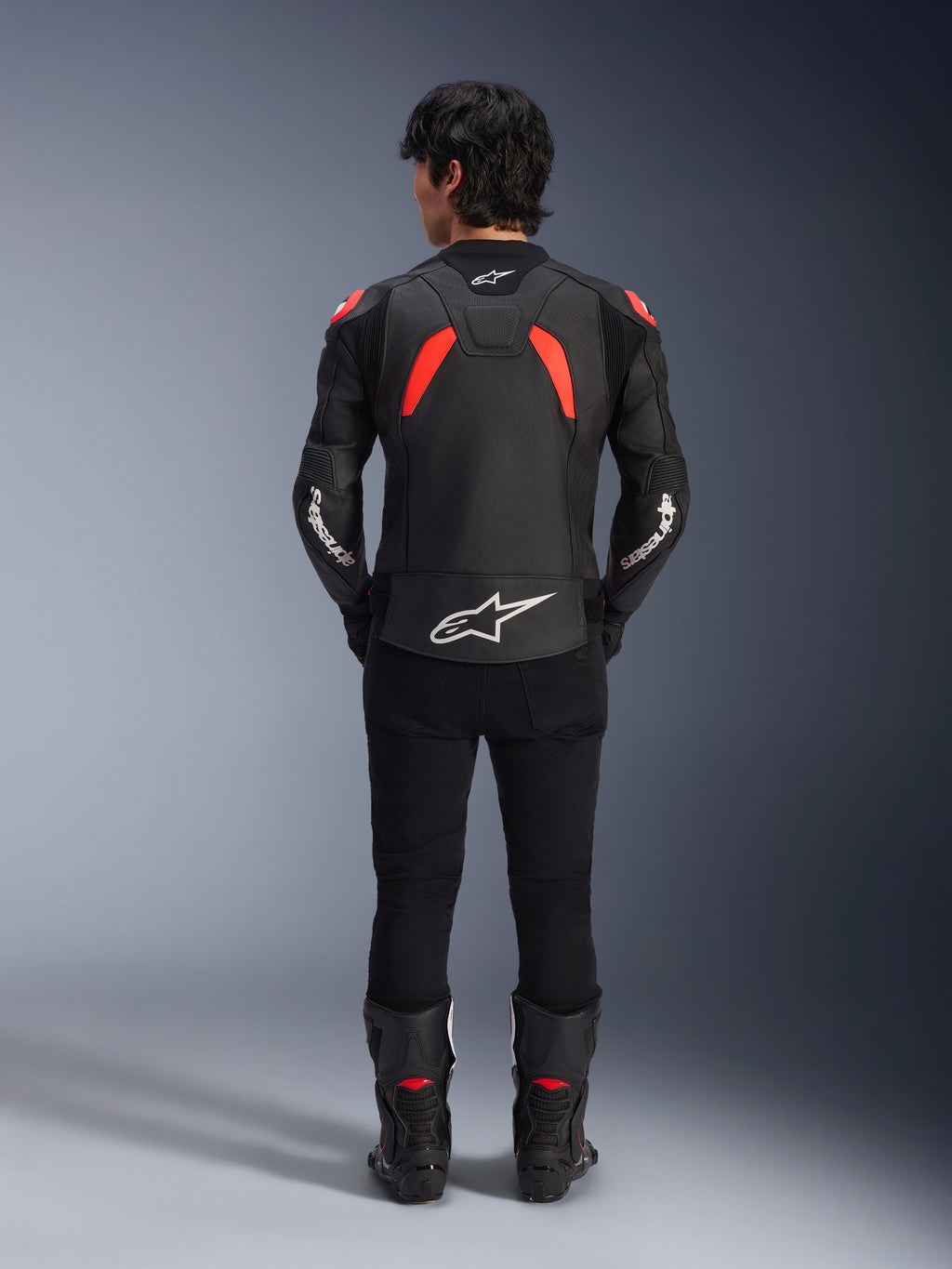Alpinestars GP Plus R V4 Airflow læderjakke, sort, rød fluo og hvid, set bagfra på en model, med perforerede læderpaneler og markant hvid branding, stylet med sorte motorcykelbukser og støvler