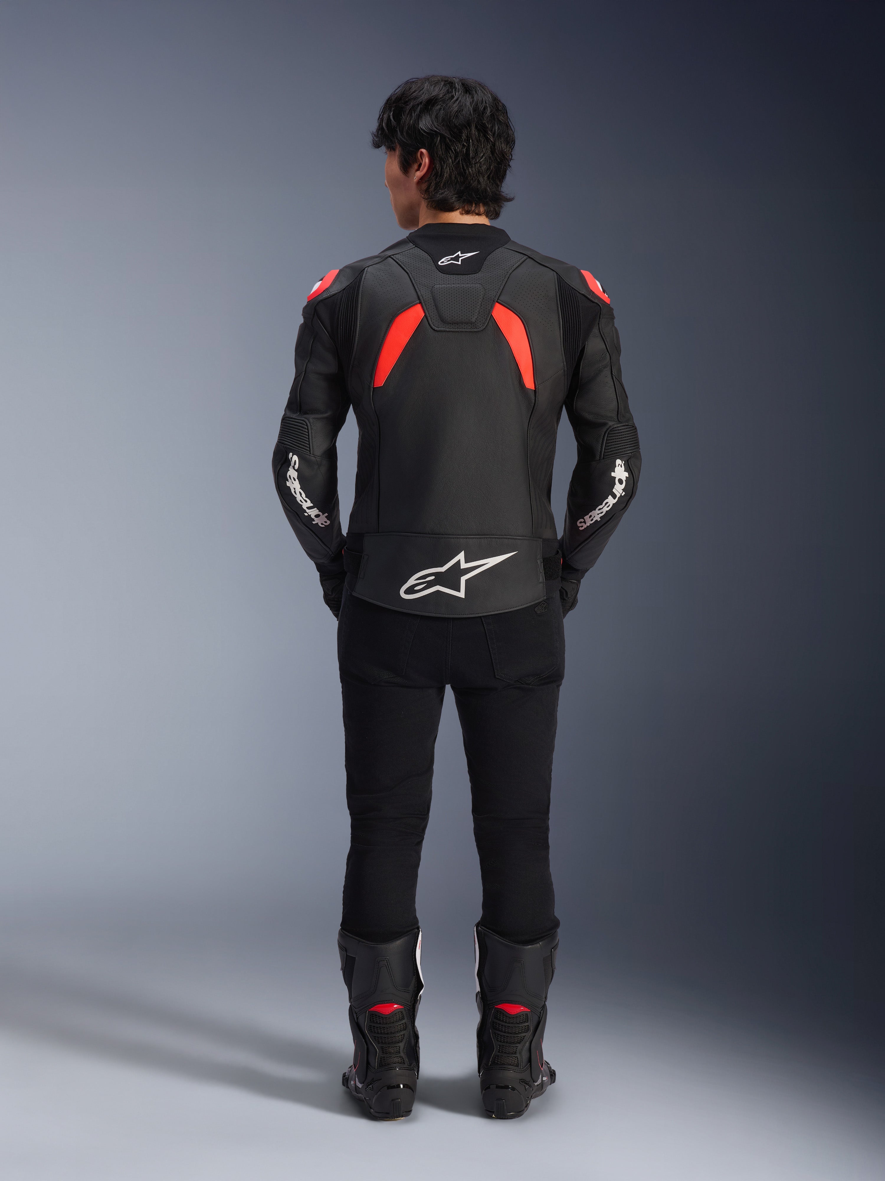 Alpinestars GP Plus R V4 Airflow læderjakke, sort, rød fluo og hvid, set bagfra på en model, med perforerede læderpaneler og markant hvid branding, stylet med sorte motorcykelbukser og støvler