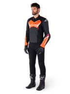 Mandlig motorcyklist iført Alpinestars Faster V3 læderjakke i sort og fluorescerende rød, kombineret med sorte kørebukser, handsker og støvler, race-inspireret silhuet med markante røde detaljer på bryst og ærmer, hvid Alpinestars branding, førsteklasses læderkonstruktion