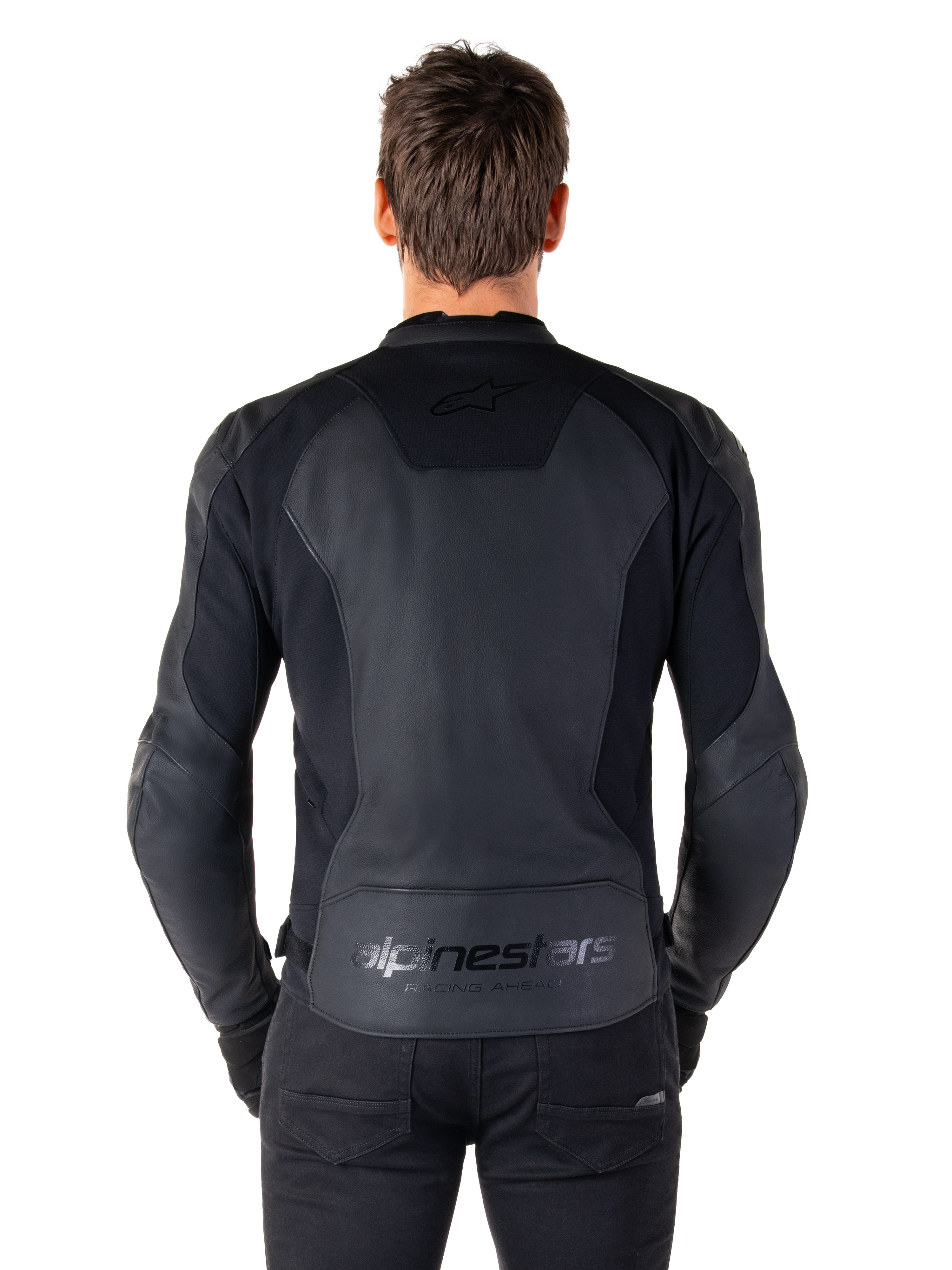 Set bagfra af en mand iført Alpinestars Faster V3 læderjakke i Black Black, med premium læderpaneler og fleksible strækindsatser, diskret 'alpinestars' og 'RACING AHEAD' branding på den nederste del af ryggen, atletisk sportspasform til motorcykelkørsel.