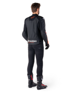 Alpinestars Faster V3 Airflow læderjakke, sort og rød fluo, set bagfra på en kører, med perforerede læderpaneler og tydelig branding, båret med sorte bukser og motorcykelstøvler, sportsbeklædning til motorcykel