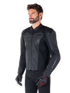 Model iført Alpinestars Faster V3 Airflow læderjakke i Black Black, sportskørejakke til motorcykel med perforeret læder og strækpaneler, kombineret med sorte bukser og sorte handsker med røde detaljer, strømlinet race-inspireret stil.