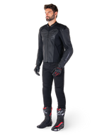 Mand iført Alpinestars Faster V3 Airflow læderjakke i Black Black, kombineret med sorte bukser, sorte og røde motorcykelhandsker og sorte racestøvler med røde og hvide detaljer, komplet sportsudstyr til kørsel
