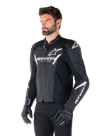 Alpinestars Faster V3 Airflow læderjakke, sort og hvid, sport-motorcykeljakke med perforerede læderpaneler, hvidt Alpinestars-branding på bryst og arme, båret af en model med sorte handsker og bukser, strømlinet og beskyttende køreudstyr