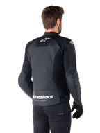 Alpinestars Faster V3 Airflow læderjakke, sort og hvid, set bagfra på en model, med perforeret læderryg for ventilation, hvide Astars-logoer på den øverste del af ryggen og nederst på lænden med 'Racing Ahead'-tekst, sporty design med strækpaneler til motorcykelbrug.