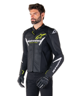 Alpinestars Faster V3 Airflow læderjakke, sport-motorcykeljakke, sort, hvid og gul fluo, båret af en mand, med perforeret læder for optimal luftstrøm, Alpinestars-logoer på bryst og arme, kombineret med sorte handsker.