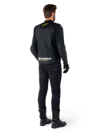 Alpinestars Faster V3 Airflow læderjakke set bagfra, sort med hvide og gul fluo-detaljer, kombineret med sorte bukser og støvler, med perforeret læder for ventilation og markant 'RACING AHEAD' branding på den nederste del af ryggen.