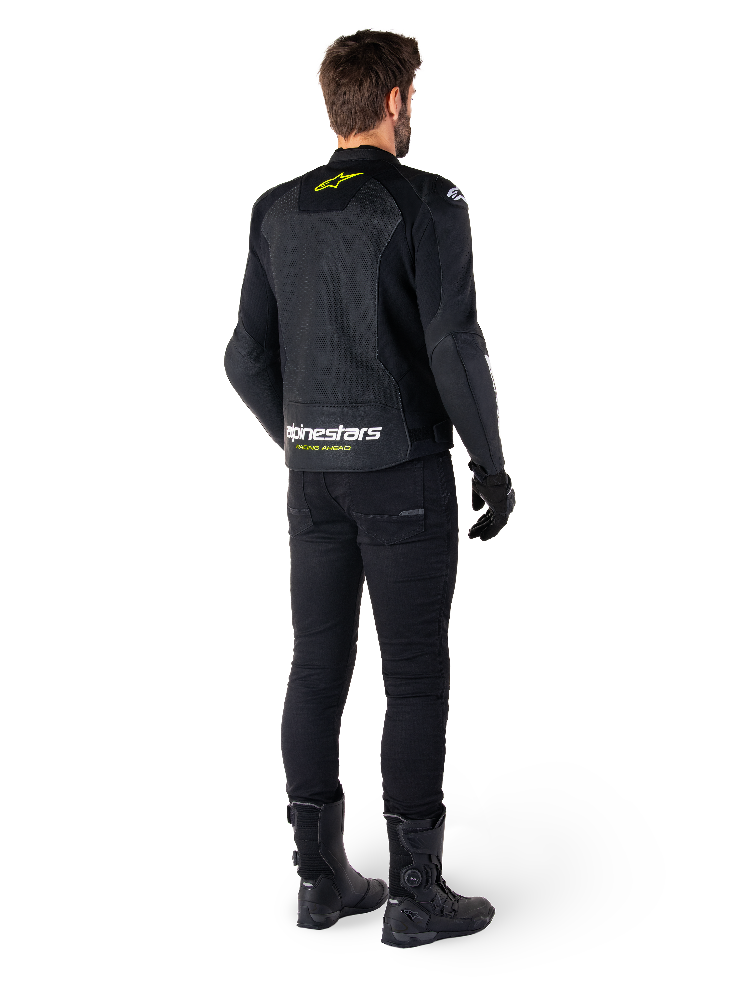 Alpinestars Faster V3 Airflow læderjakke set bagfra, sort med hvide og gul fluo-detaljer, kombineret med sorte bukser og støvler, med perforeret læder for ventilation og markant 'RACING AHEAD' branding på den nederste del af ryggen.