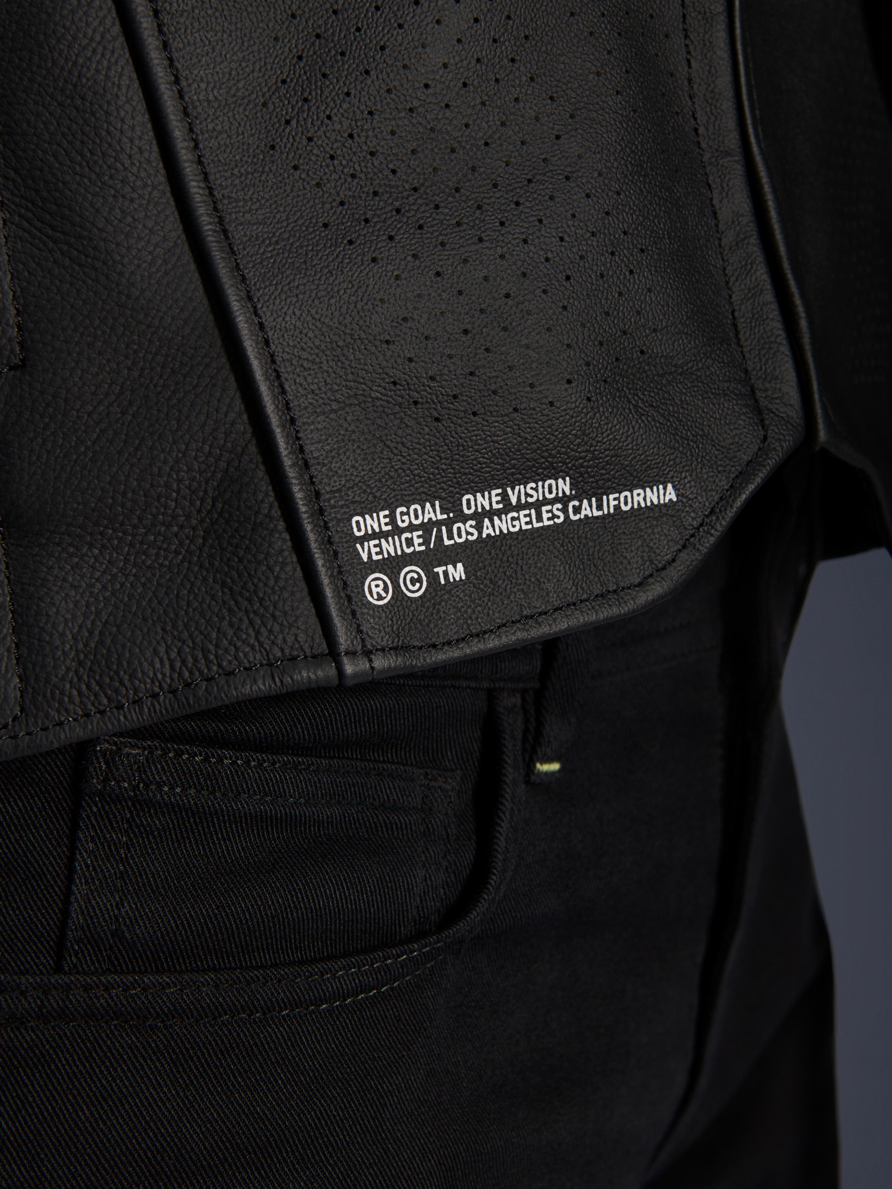 Nærbillede af Alpinestars Atem V5 læderjakken i sort, der viser det nederste rygpanel med 'ONE GOAL. ONE VISION. VENICE / LOS ANGELES CALIFORNIA' branding og perforeret lædertekstur.